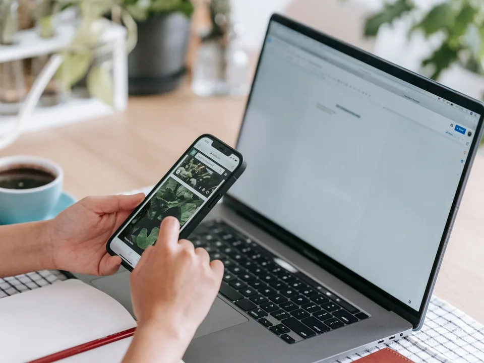 Person browsing product photos on a phone beside an open laptop, the kind of return visit a Meta retargeting ad prompts