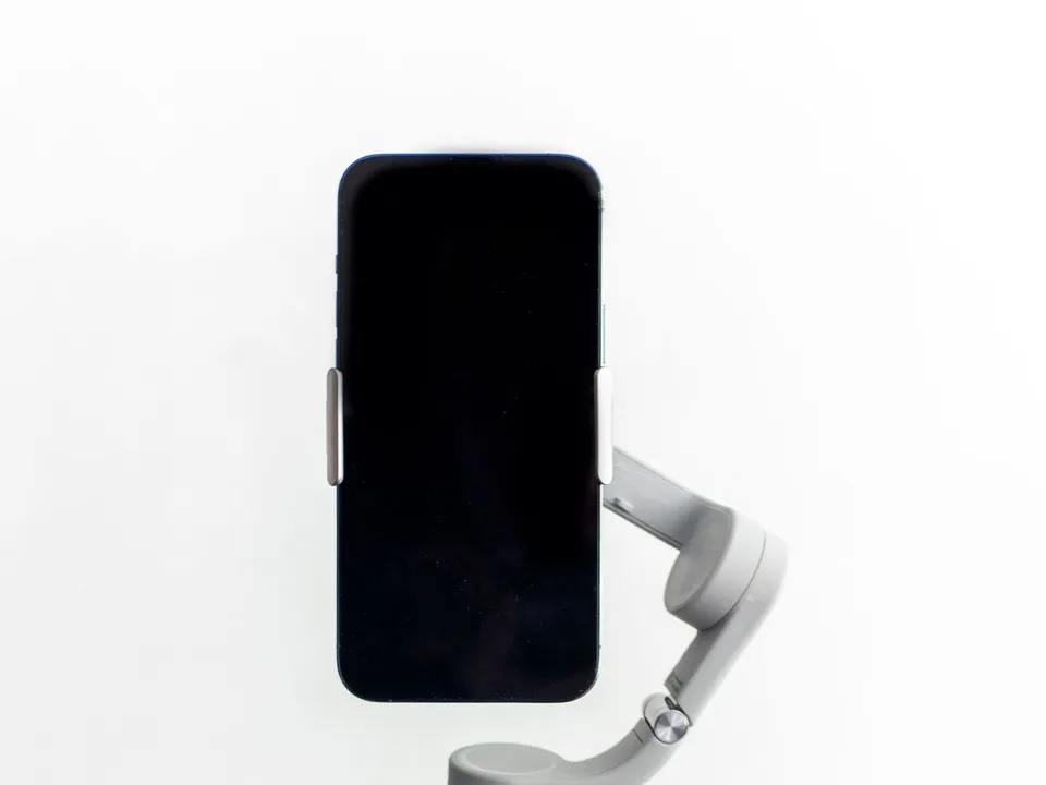 Smartphone mounted on a handheld gimbal stabiliser against a white wall, ready to film a vertical Reel