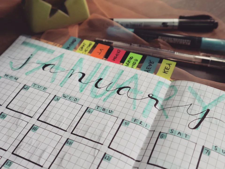 Hand-lettered monthly planner page with coloured sticky tabs, the kind of calendar a social media manager fills a month ahead